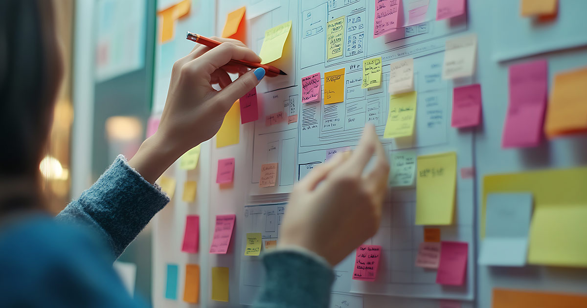 Designer-Mapping-out-UX-UI-Design-with-postits-and-wireframes-on-a-whiteboard